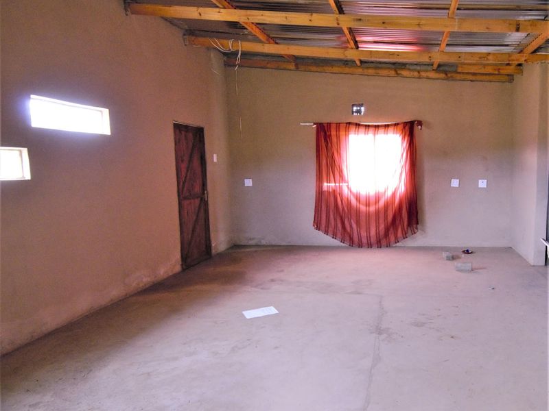 An unfinished, open-plan living area featuring exposed timber roof trusses, corrugated metal roofing, and cement screed flooring.