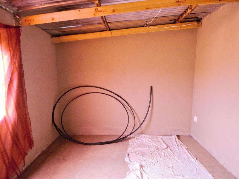 An unfinished interior room featuring exposed timber rafters and corrugated metal ceiling, offering a blank canvas for renovation and completion.