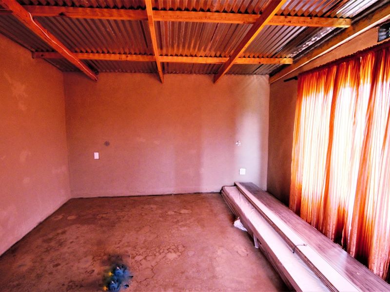 An unfinished bedroom space featuring exposed timber rafters, a corrugated metal roof, and concrete flooring, offering a blank canvas for renovation.
