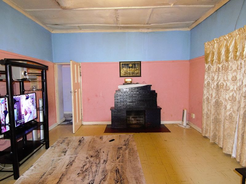 Living room featuring a central brick fireplace, timber flooring, and a tiled ceiling with visible signs of wear and water damage.