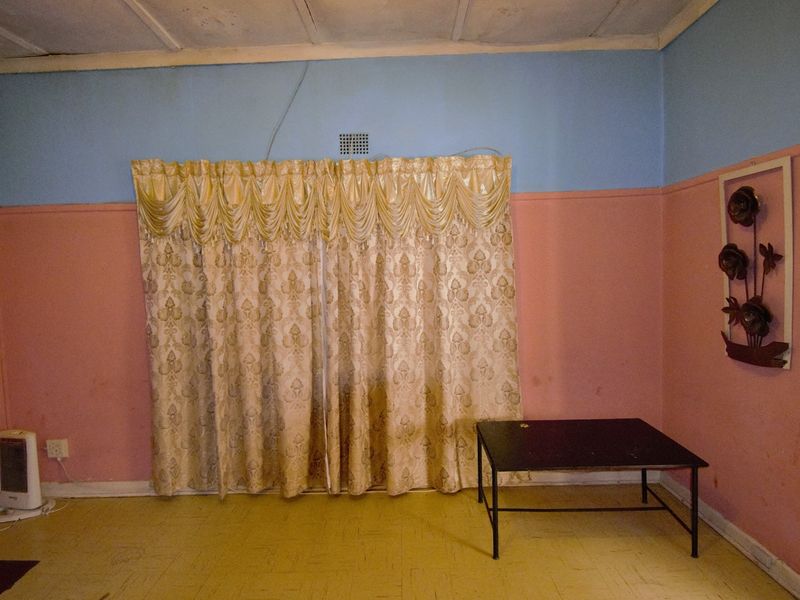 A sparsely furnished living room featuring two-tone wall paint and standard floor tiling, requiring cosmetic updates to modernize the space.