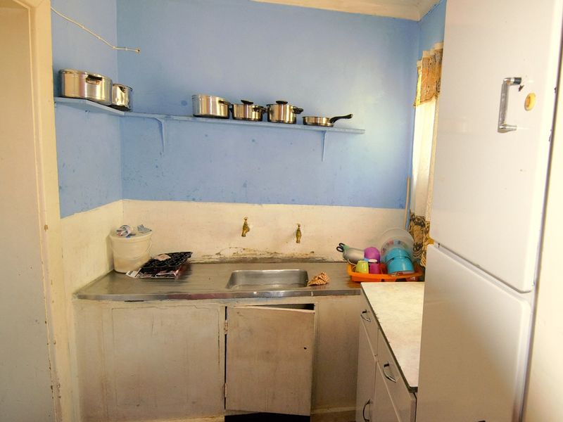 A compact scullery area featuring a stainless steel sink, wall-mounted taps, and basic built-in cabinetry with open shelving.