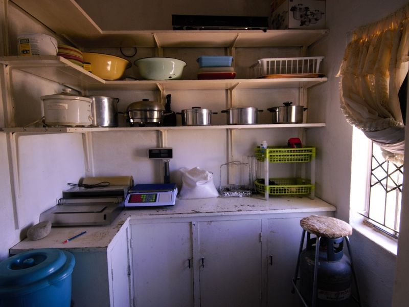 A functional scullery or utility prep area featuring built-in cabinetry, open shelving, and a window with security bars.