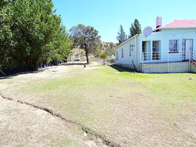 Rear view of the property featuring a large lawn area, metal roof, and elevated access stairs with security railings.