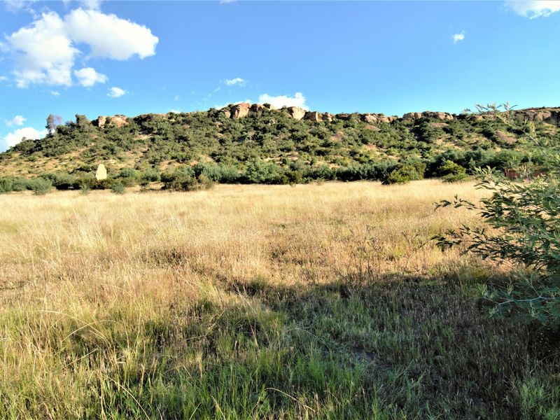 A wide-angle view of a vacant residential plot featuring natural grassland and a scenic rocky hillside backdrop.