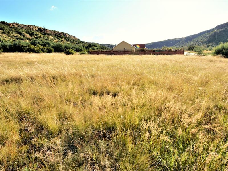 A wide-angle view of a vacant residential plot featuring natural grassland, surrounded by scenic hills and neighboring residential properties.