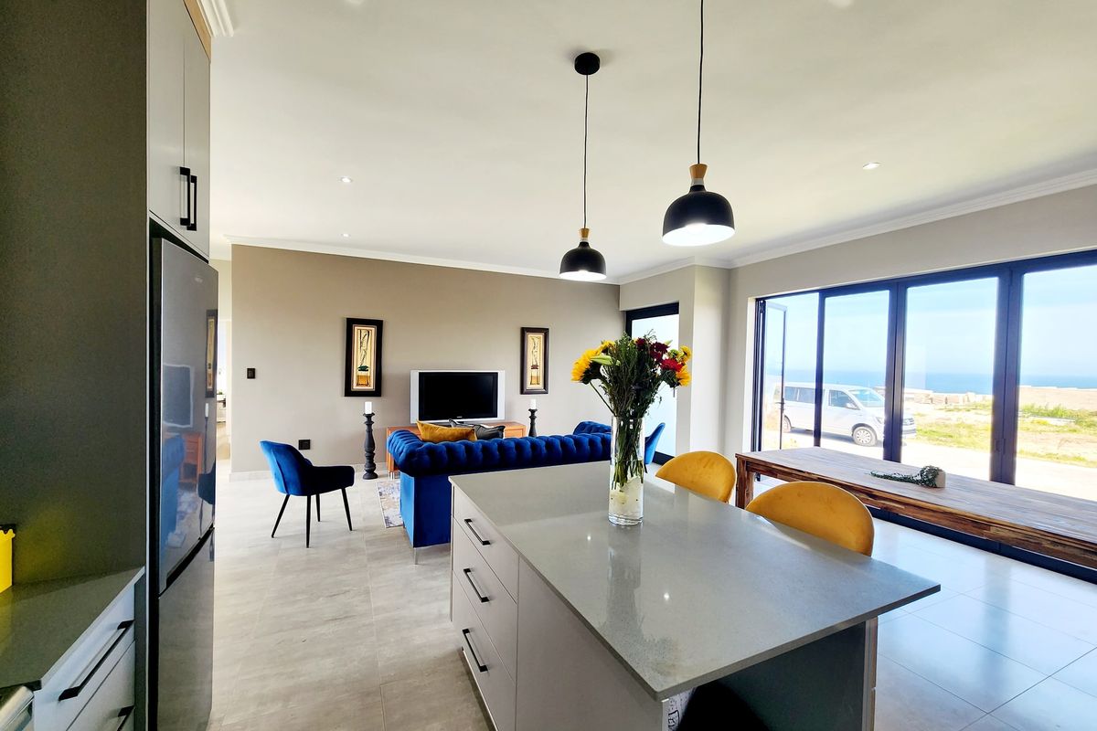 Modern open-plan living area featuring a sleek kitchen island with quartz countertops, recessed lighting, and large sliding glass doors leading to an outdoor view.