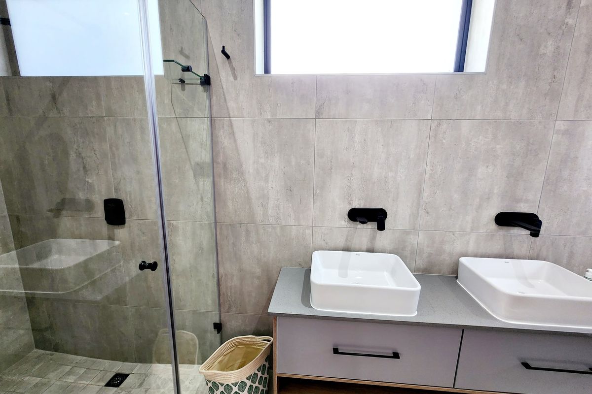 Modern bathroom featuring a double vanity with vessel sinks, wall-mounted matte black faucets, and a spacious walk-in shower with glass enclosure.