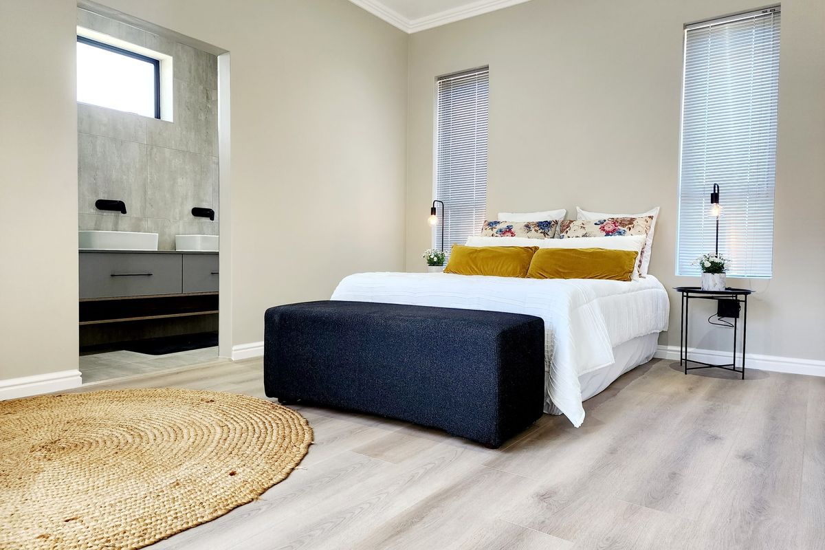 A modern, well-maintained bedroom featuring light laminate flooring, neutral walls, and an open-plan en-suite bathroom with a contemporary double vanity.