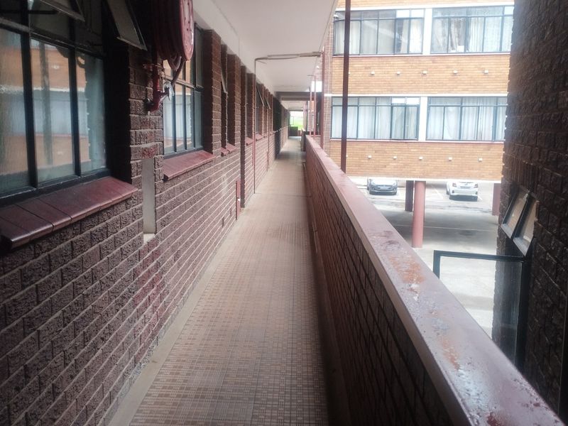 An exterior apartment building walkway featuring brick walls, tiled flooring, and a metal safety railing overlooking the parking area.