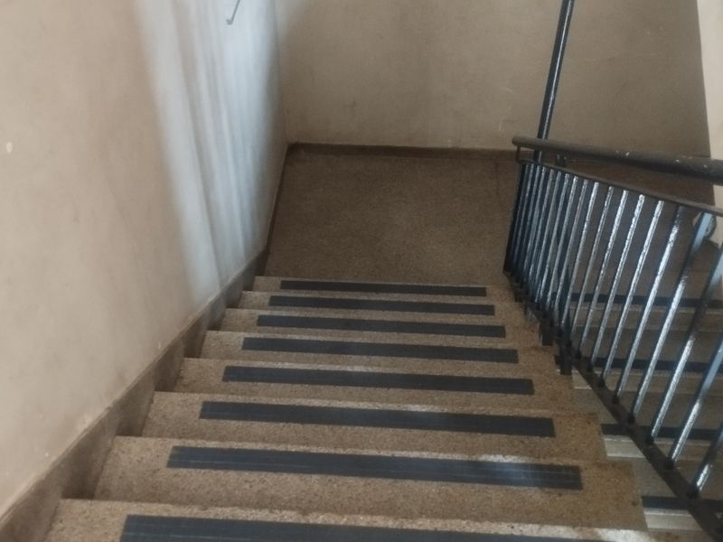 A functional concrete staircase featuring a black metal handrail and anti-slip stair treads, providing access within the apartment building.