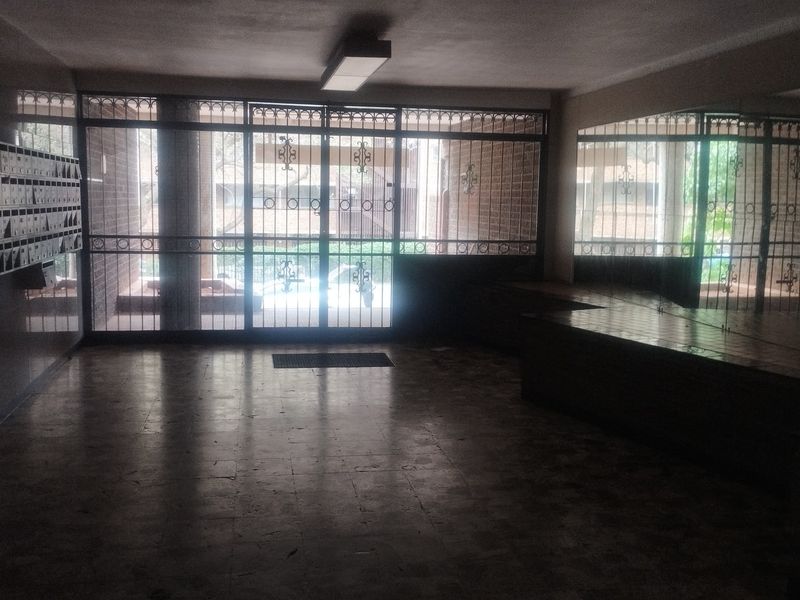 A spacious apartment building entrance lobby featuring tiled flooring, a wall of mailboxes, and large security-gated glass doors.
