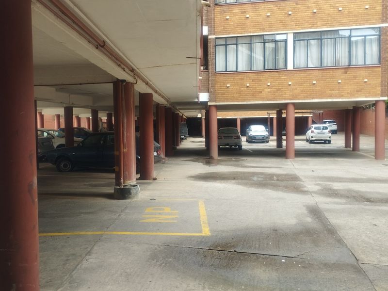 Covered parking area featuring concrete columns and a concrete slab ceiling, located beneath the apartment building structure.