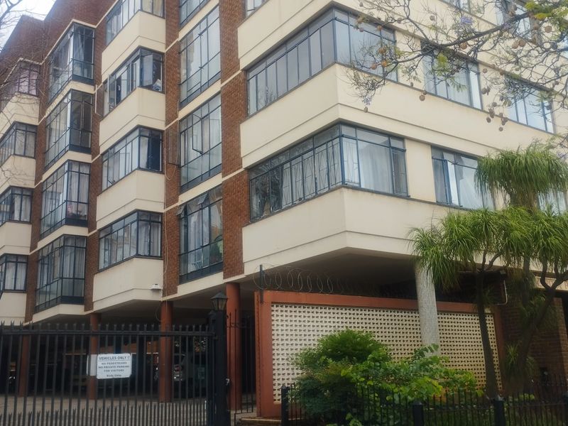 Exterior view of a multi-story apartment building featuring brick and plaster facade with steel-framed windows and secure gated entrance.