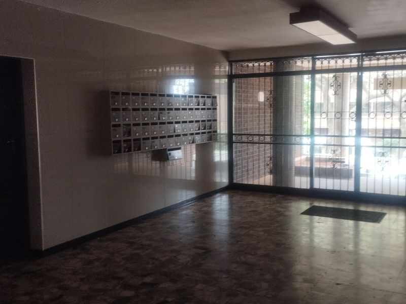 A communal apartment building entrance lobby featuring tiled flooring, wall-mounted mailboxes, and a secure glass entrance door.