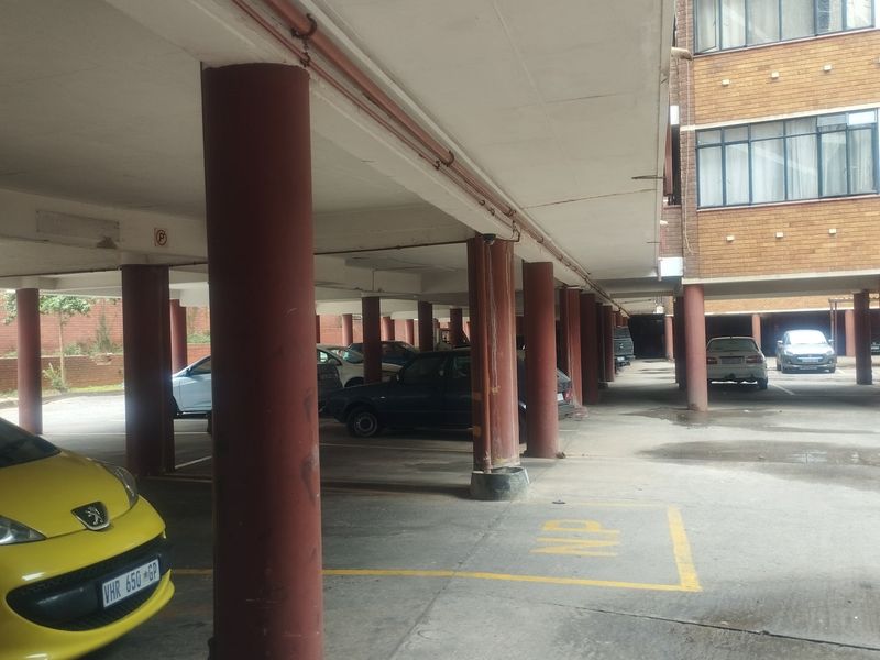 Covered parking area featuring concrete columns and flooring, providing sheltered vehicle storage for the apartment complex.