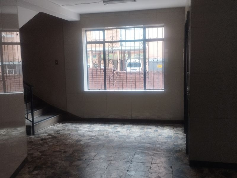 A vacant hallway area featuring tiled flooring, a staircase, and a window fitted with security bars.