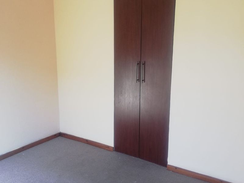 An empty bedroom featuring neutral walls, carpeted flooring, and a dark wood-finish built-in cupboard.