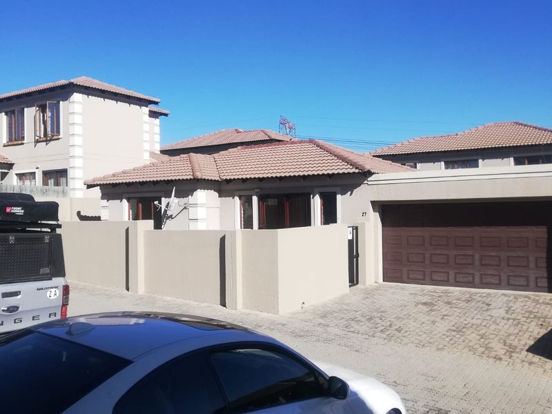 Front exterior view of a townhouse featuring a paved driveway, a secure perimeter wall, and a double garage.