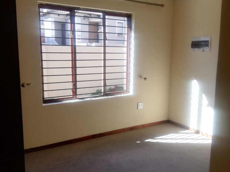 An empty bedroom featuring carpet flooring, a window with security burglar bars, and a wall-mounted electrical distribution board.