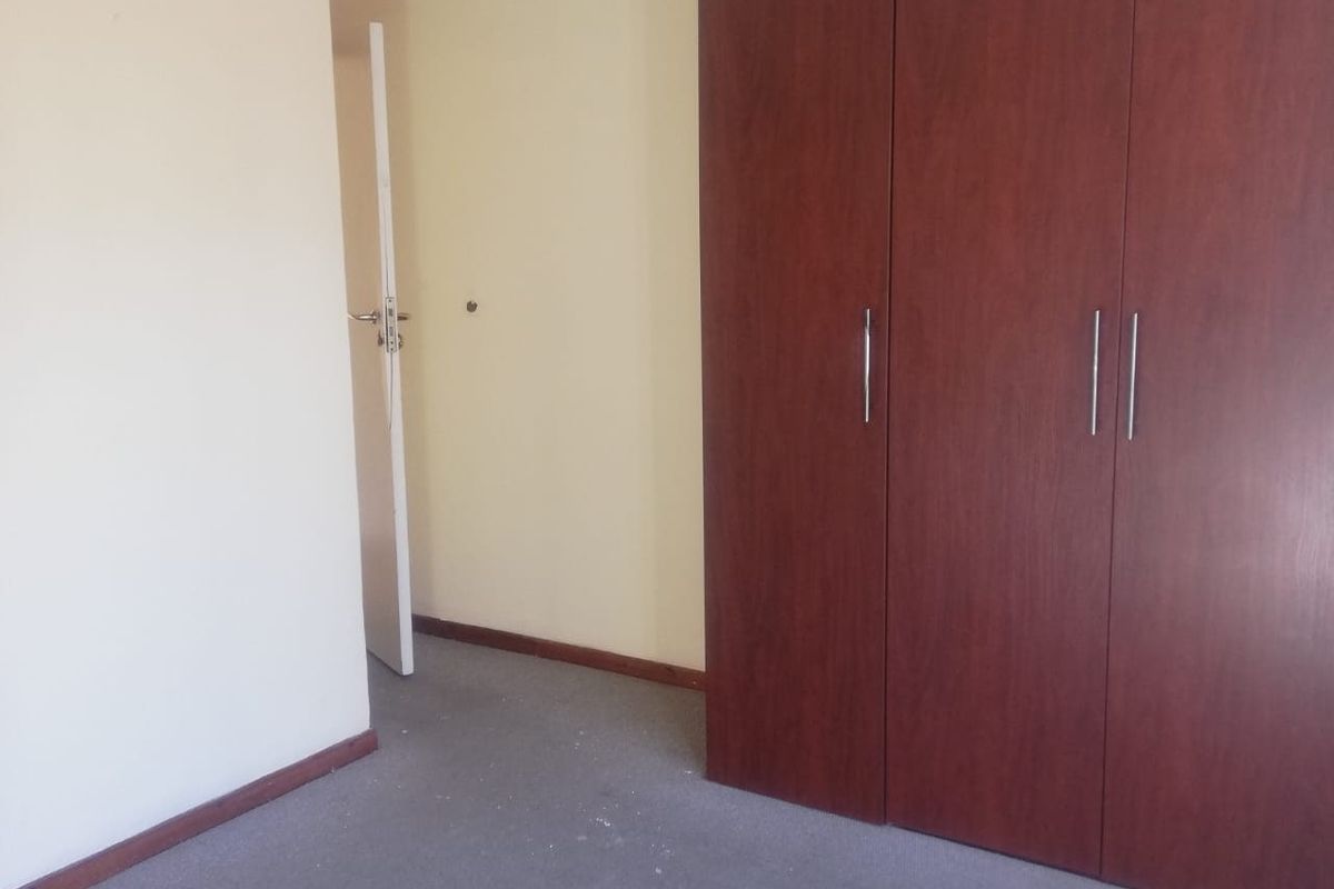 An empty bedroom featuring built-in wooden cupboards and carpeted flooring, offering a blank canvas for personalization.
