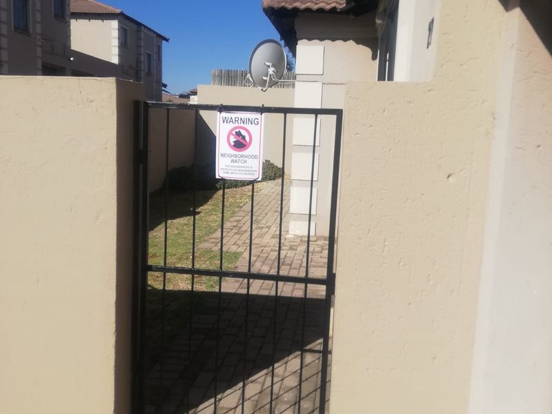 A gated entrance leading to a paved walkway and side garden area of the townhouse property.