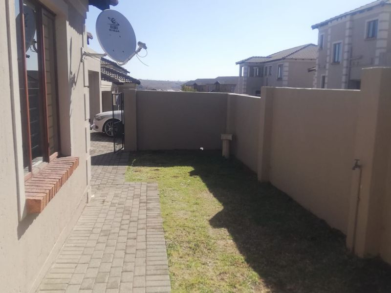 A side view of the townhouse featuring a paved walkway, a small grassed area, and a secure boundary wall.