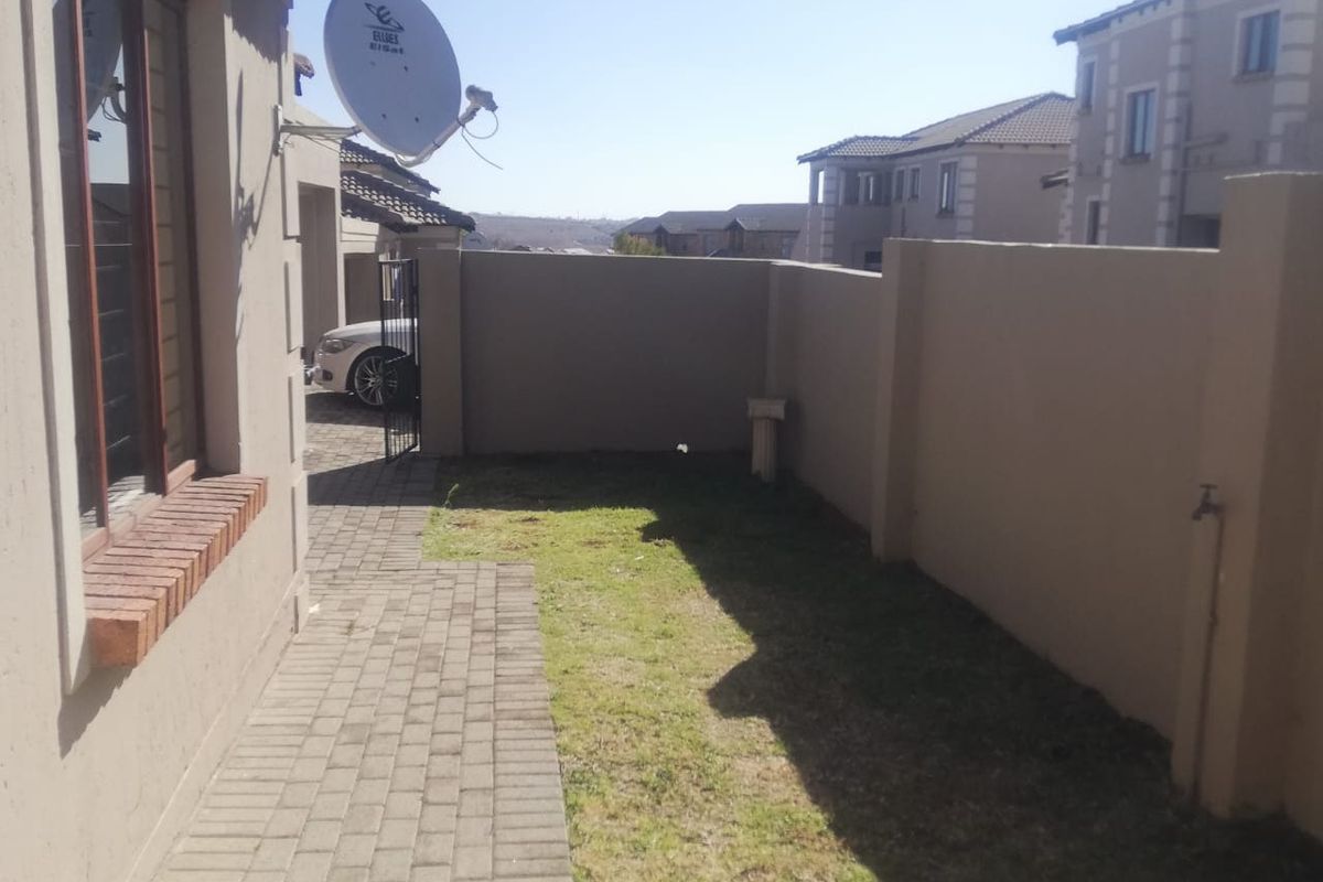 A side view of the townhouse featuring a paved walkway, a small grassed area, and a secure boundary wall.