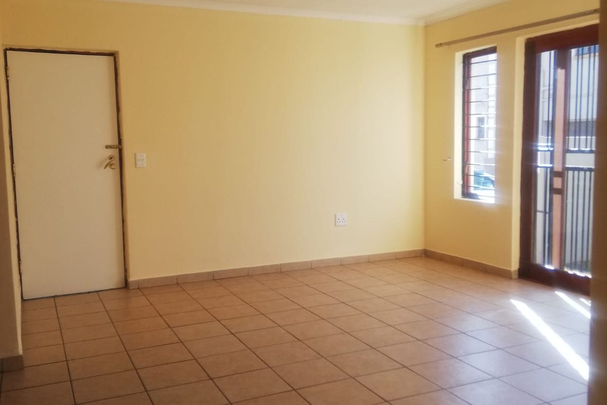 An empty, tiled living room featuring recessed lighting, a security gate, and access to an outdoor area through a sliding door.