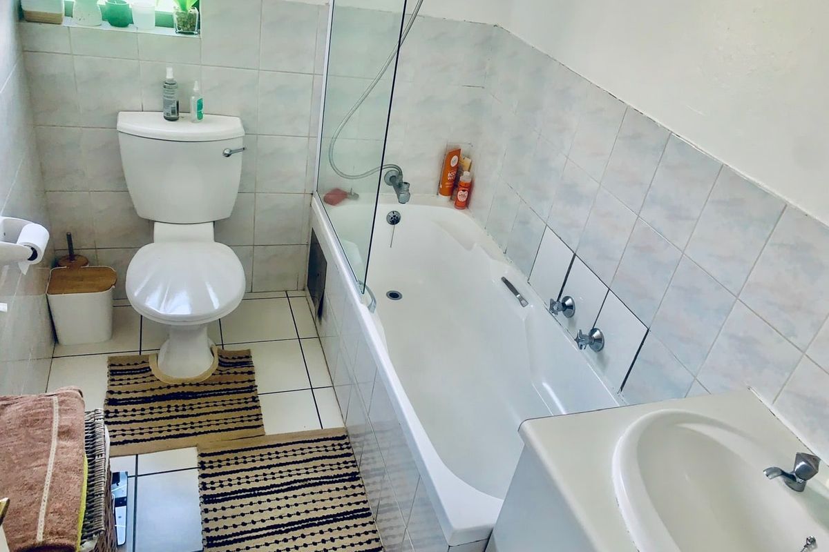 A functional bathroom featuring a bathtub with a glass shower screen, a toilet, and a vanity basin with tiled finishes throughout.