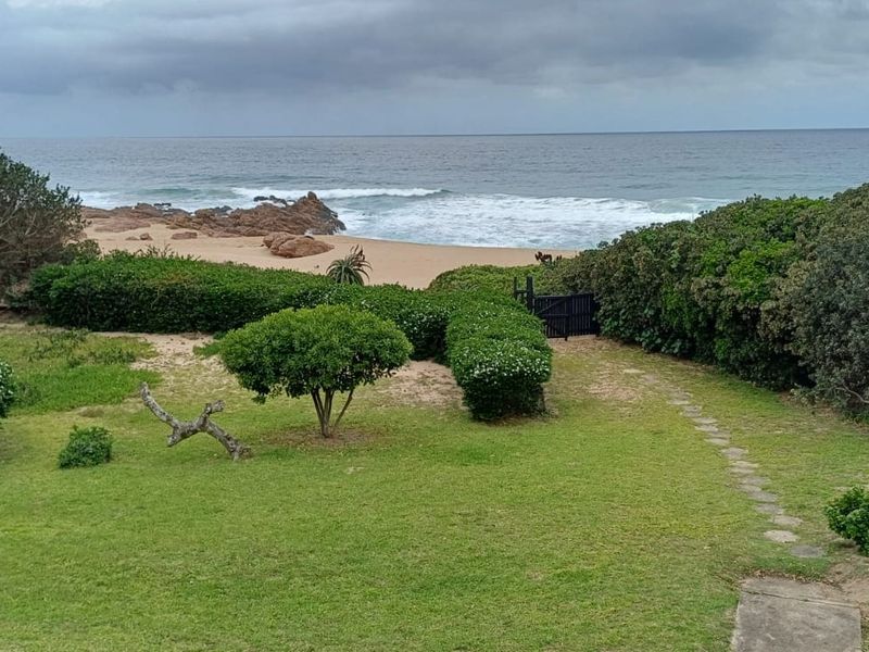 A scenic view of a well-maintained garden with a stone pathway leading directly to the beach and ocean.