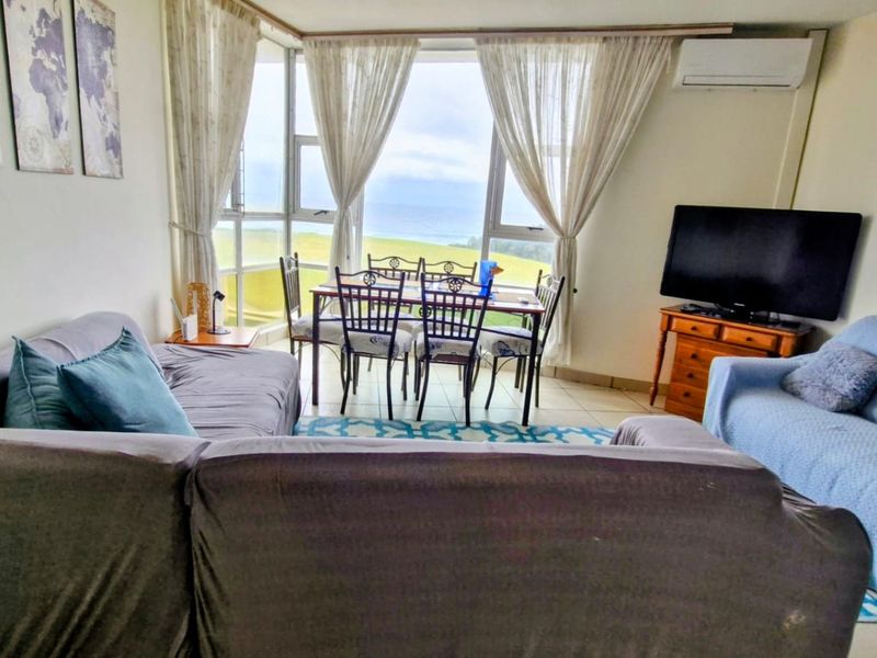 Open-plan living and dining area featuring large windows with ocean views, tiled flooring, and a wall-mounted air conditioning unit.