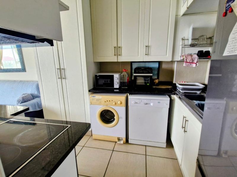 Compact kitchen featuring white cabinetry, granite countertops, ceramic tile flooring, and integrated appliances including a hob and extractor fan.