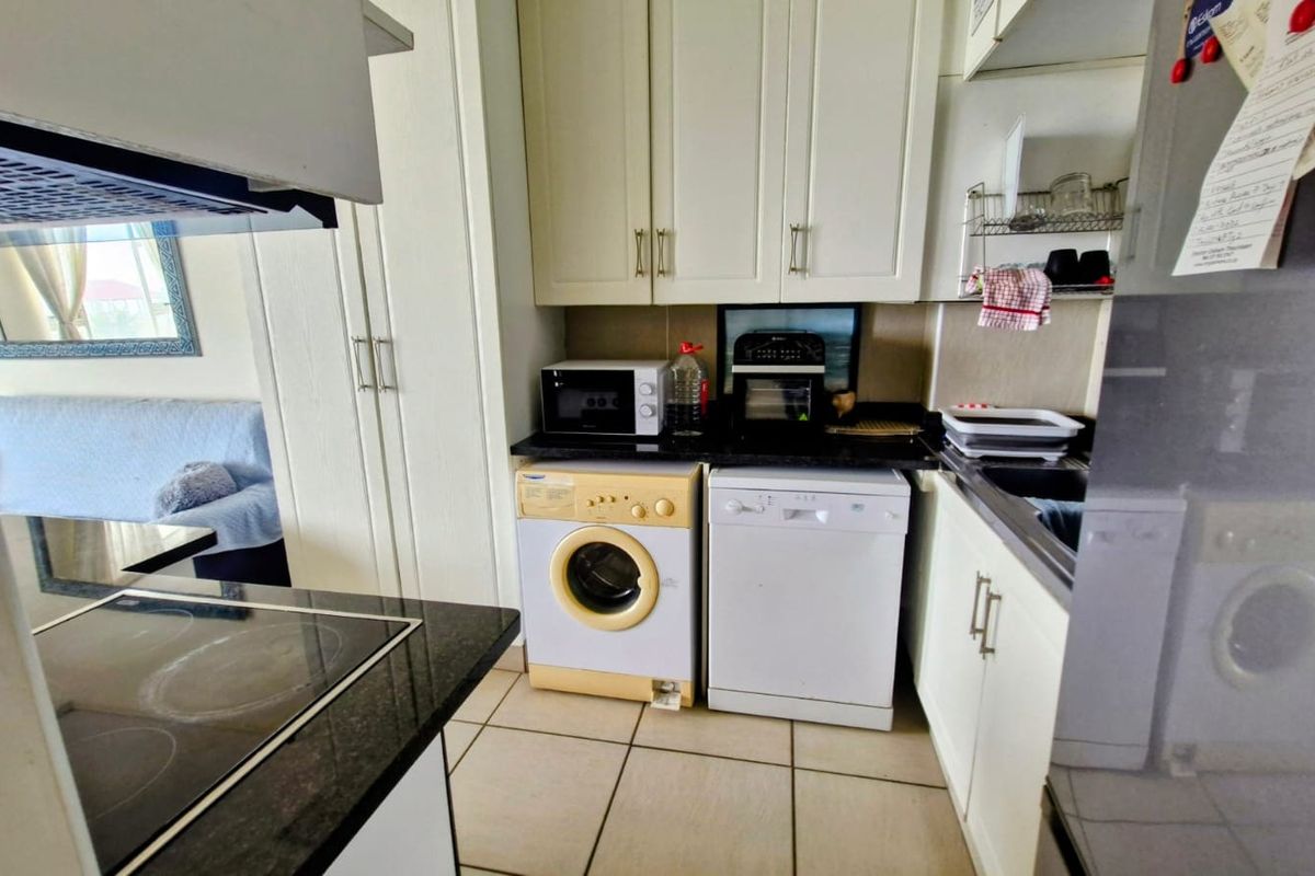 Compact kitchen featuring white cabinetry, granite countertops, ceramic tile flooring, and integrated appliances including a hob and extractor fan.