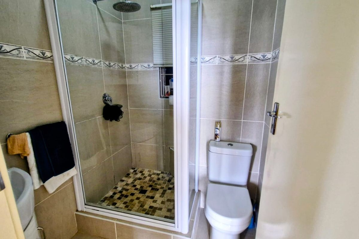 A compact bathroom featuring a tiled shower enclosure, a standard toilet, and a basin with neutral wall tiling.