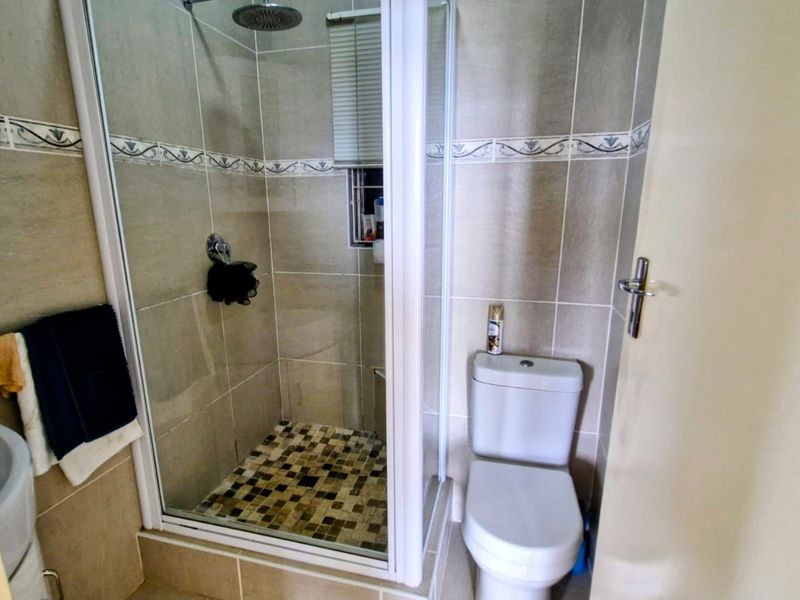 A compact bathroom featuring a tiled shower enclosure, a standard toilet, and a basin with neutral wall tiling.