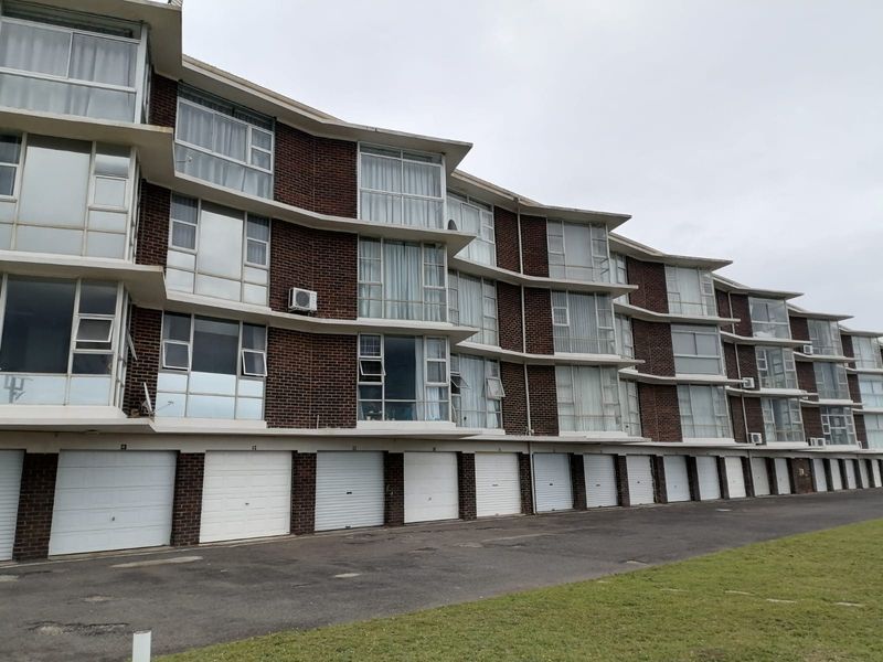 Exterior view of a multi-story apartment complex featuring a brick facade, large windows, and a row of ground-level garage doors.