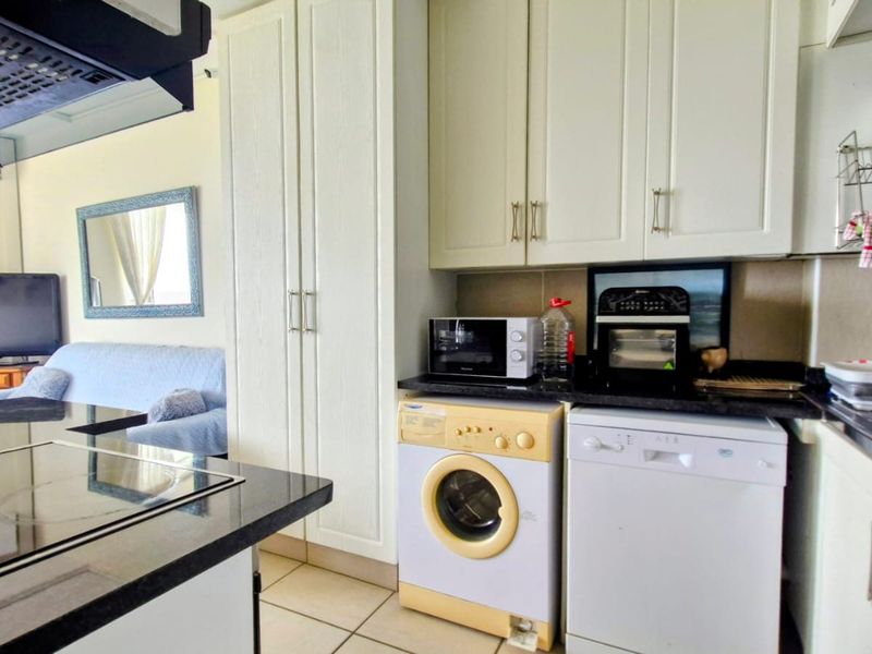 Open-plan kitchen area featuring white built-in cabinetry, granite countertops, and integrated laundry and dishwasher appliances, flowing into the adjacent living space.