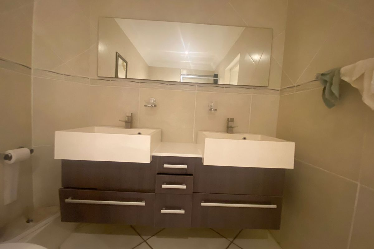 A modern bathroom featuring a double vanity with built-in cabinetry, wall-mounted mirror, and neutral tiled finishes throughout.