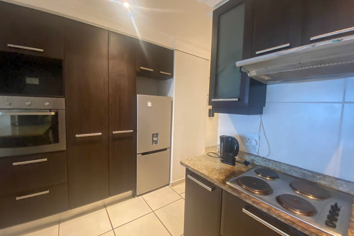 A functional kitchen featuring dark wood cabinetry, stone countertops, built-in oven, and electric hob with an integrated extractor fan.