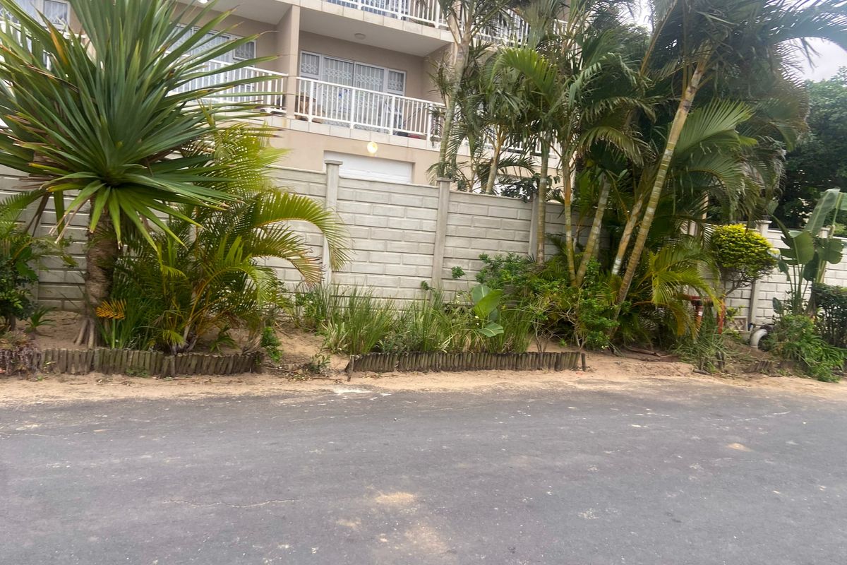 Exterior view of an apartment building featuring a precast concrete boundary wall, landscaped garden area, and balconies overlooking the paved driveway.
