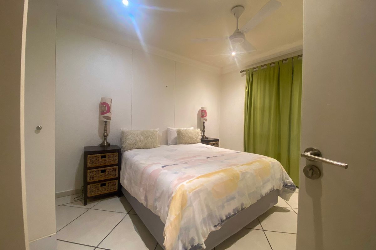 A functional bedroom featuring tiled flooring, a ceiling fan, and built-in storage, offering a clean and neutral space for rest.