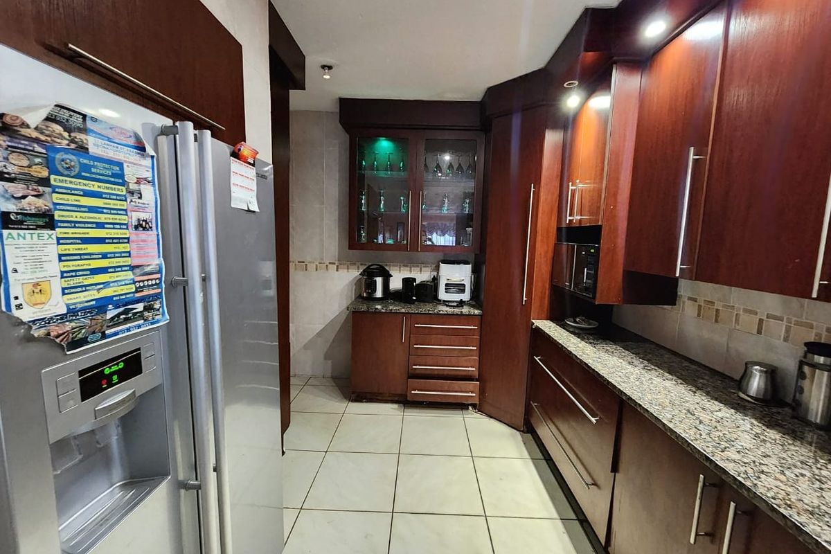 A functional kitchen featuring dark wood cabinetry, granite countertops, tiled flooring, and integrated display cabinets with accent lighting.
