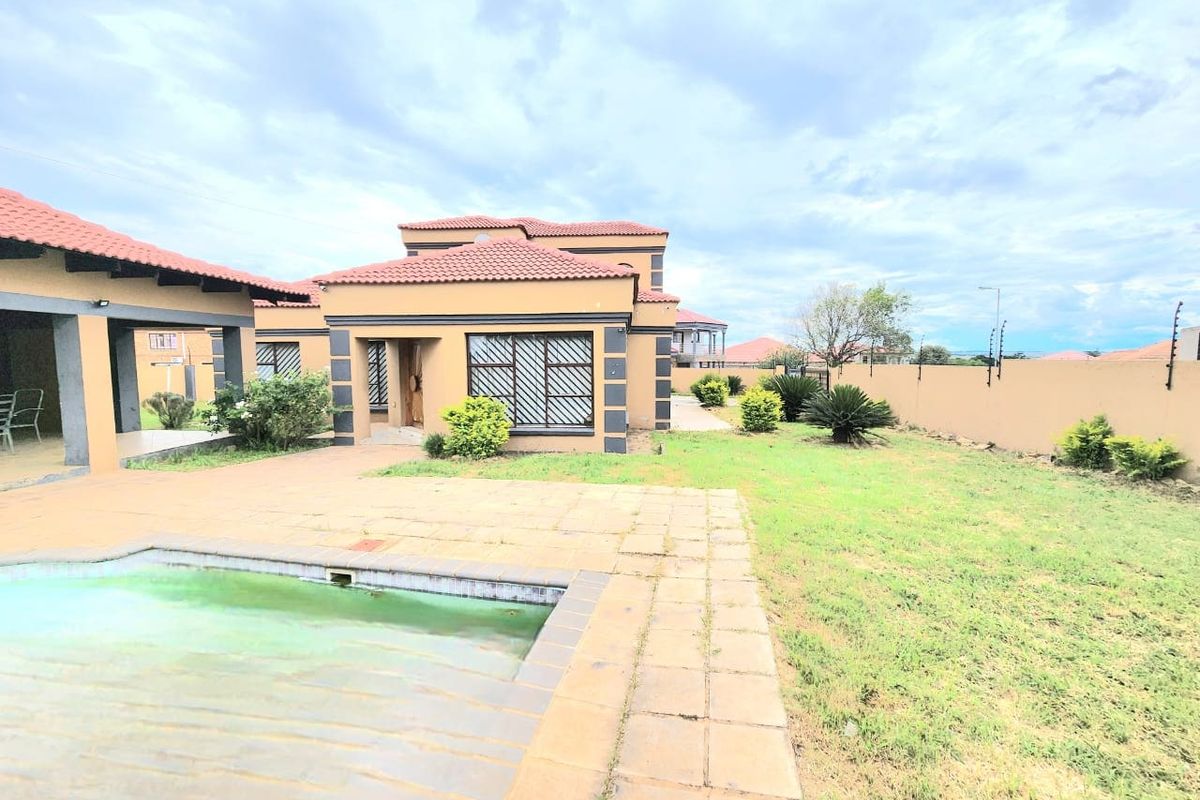 Rear view of the property featuring a swimming pool, paved patio area, and a large garden enclosed by a perimeter wall.