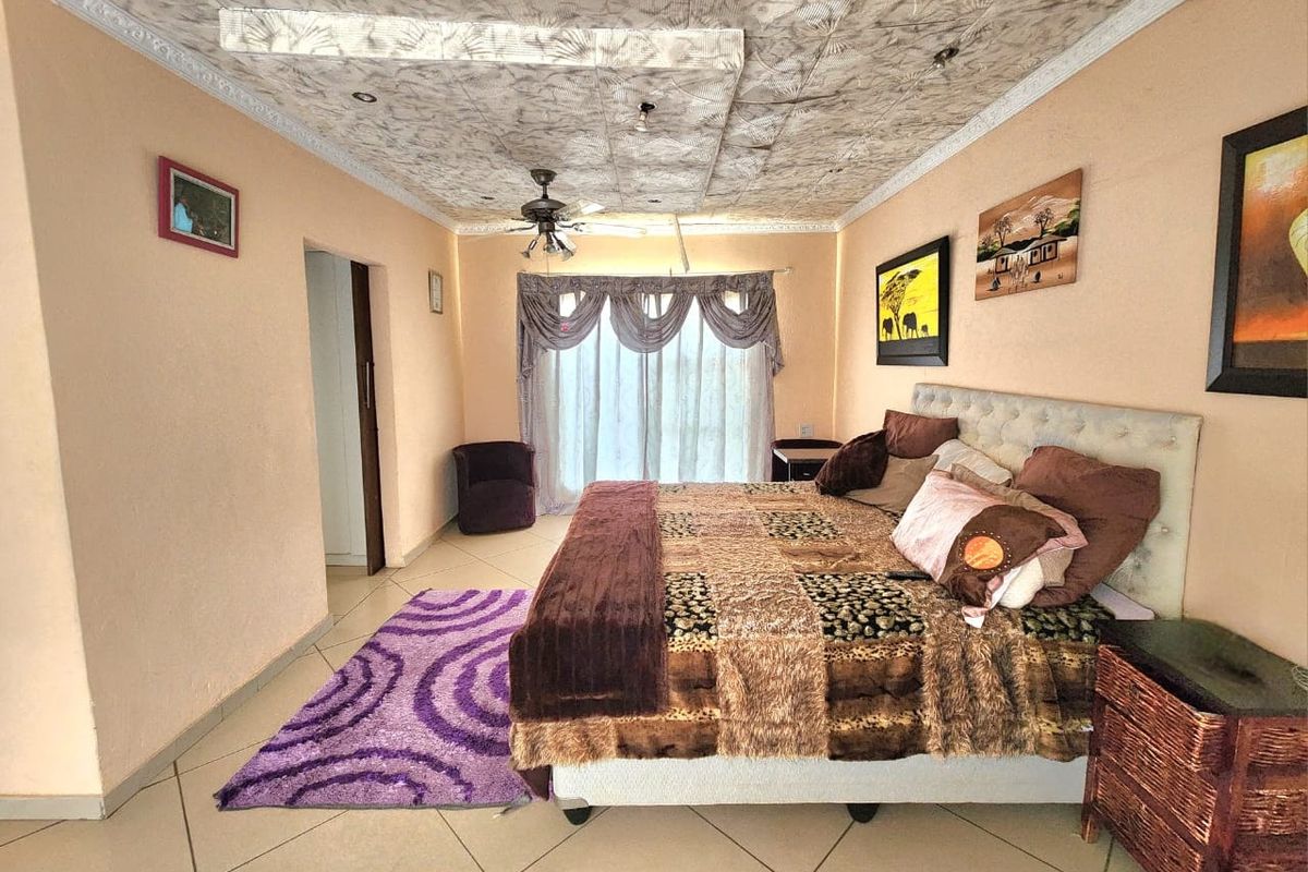 A spacious bedroom featuring tiled flooring, a ceiling fan, and a unique decorative ceiling panel with integrated lighting.