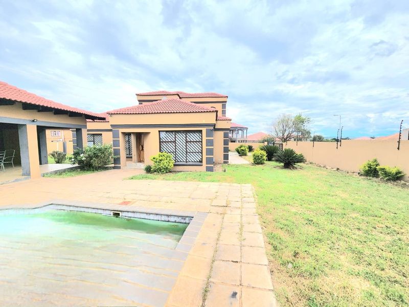 Rear view of the property featuring a swimming pool, paved patio area, and a large garden enclosed by a perimeter wall.