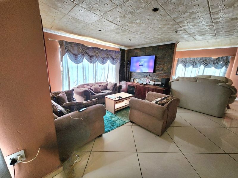 Spacious living room featuring a stone accent wall, tiled flooring, and decorative ceiling tiles, offering a comfortable layout for family relaxation.