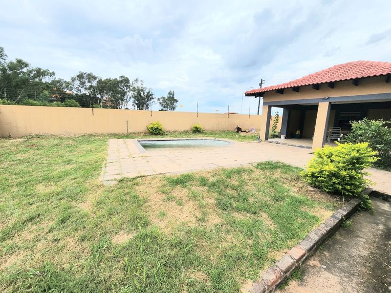 Outdoor pool area featuring a paved patio, covered entertainment space, and perimeter wall with electric fencing.