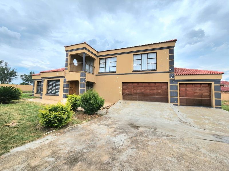 A two-story residential property featuring a double garage, tiled roof, and an upper-level balcony, set on a spacious lot with a concrete driveway.
