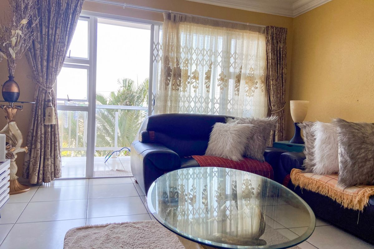A living room featuring tiled flooring and a sliding glass door with a security gate, providing access to an outdoor balcony area.